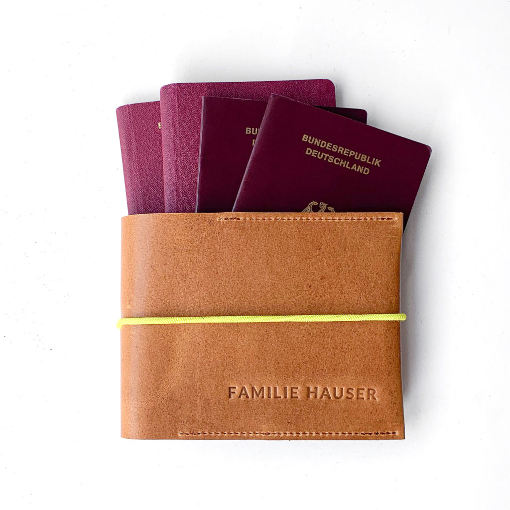 Family passport case EVE made of sustainable natural leather in cognac oiled with yellow closure band and individual embossing and four passports.