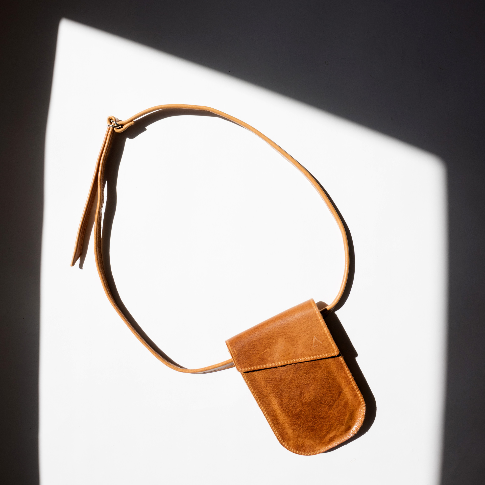 Mood Shot cell phone bag chest pouch IRA made of sustainable natural leather in cognac oiled with long strap lying in the sun