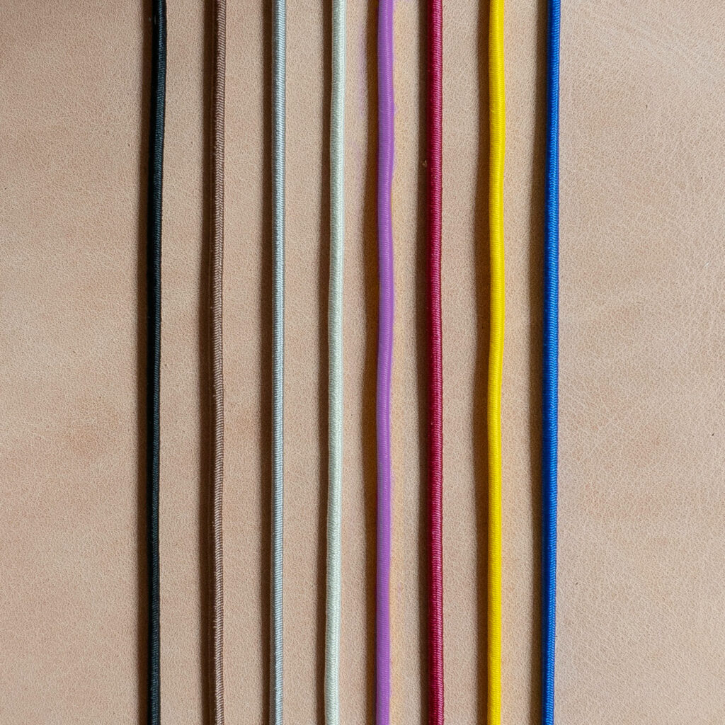Rubber bands for notebook covers in black, brown, gray, cream, red, yellow and blue on light brown, natural leather.