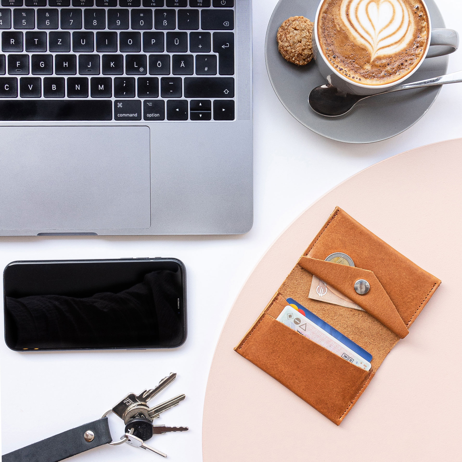 Wallet OLI MIDI in cognac oiled in size comparison with laptop, coffee cup, cell phone and keys.