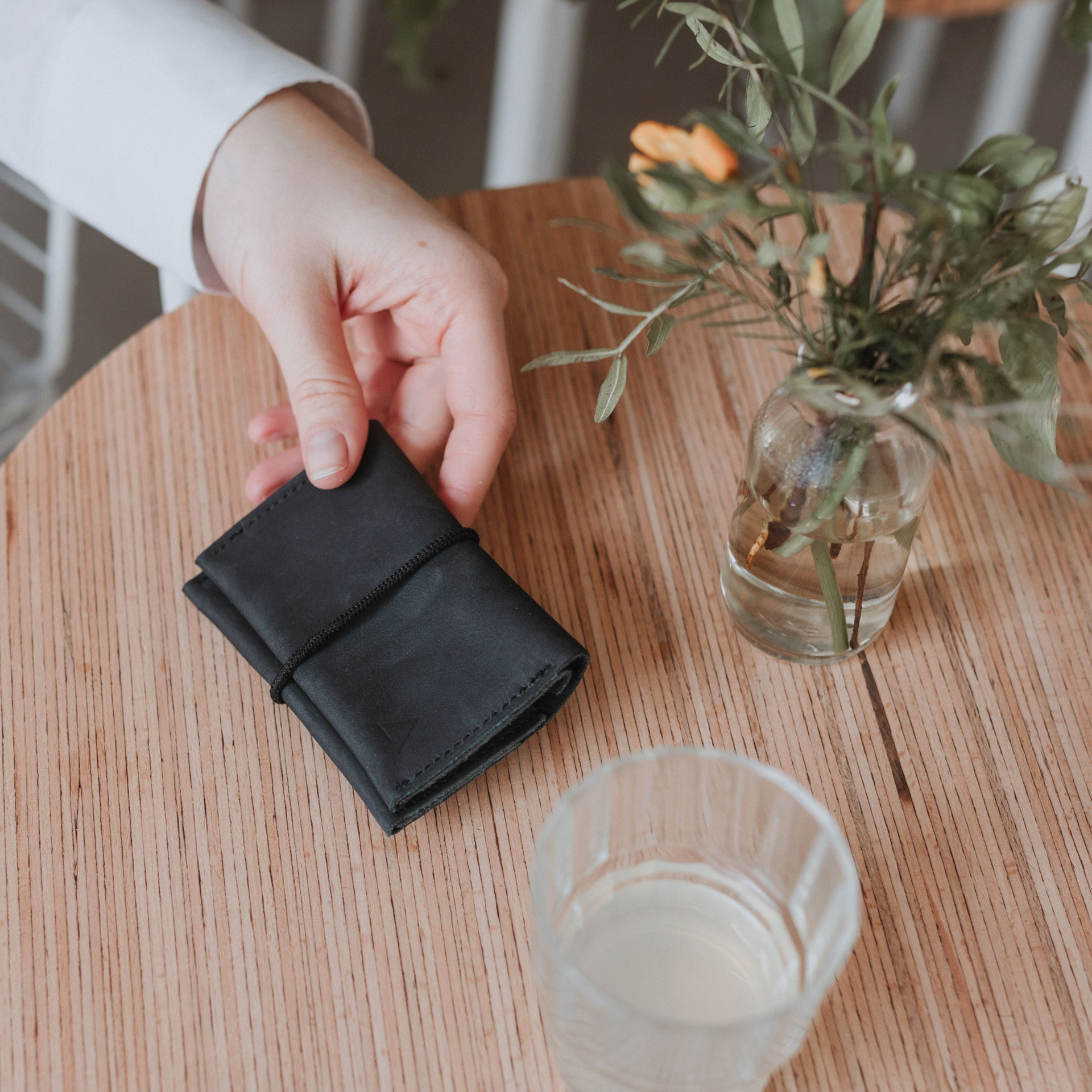 OLI natural leather wallet in charcoal with black closure band on wooden table with water glass