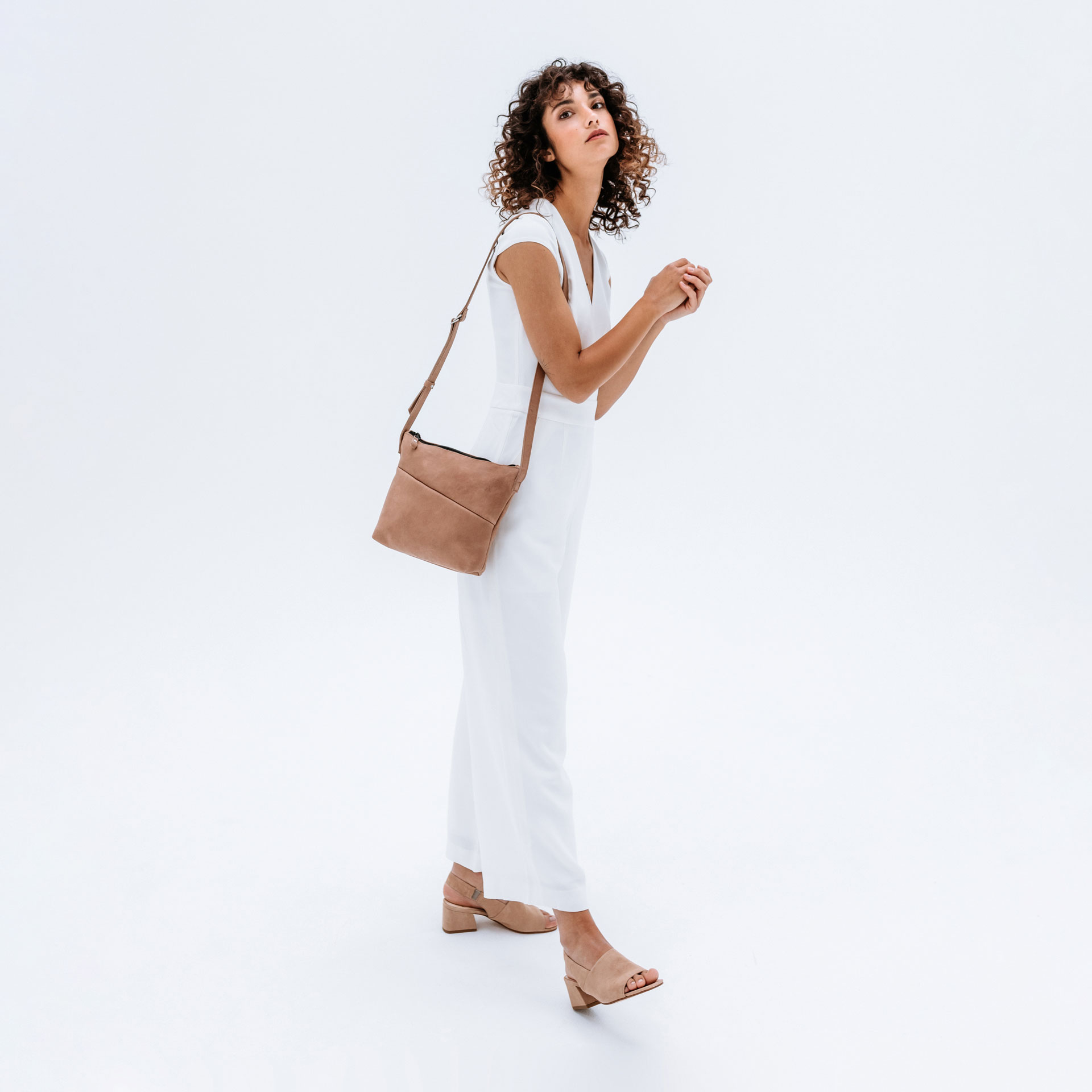Model wears shoulder bag Ida in light brown color made of natural leather over the shoulder.