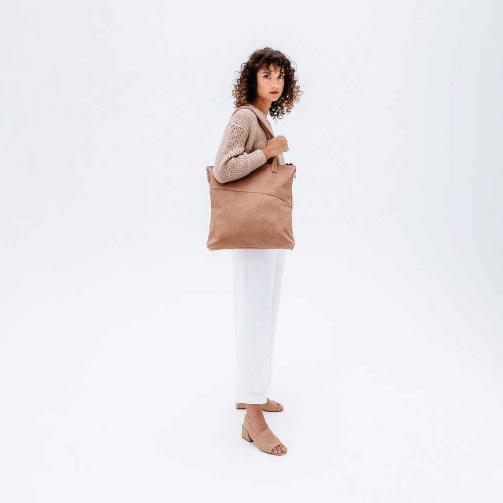 Model wears shopper Fia in light brown from sustainable natural leather over the shoulder.