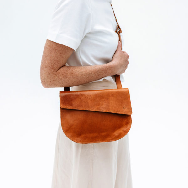 Model carries shoulder bag BEA in cognac natural leather over the shoulder.