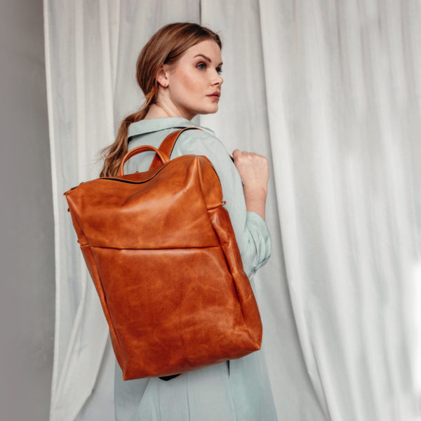 Model wears backpack NEO Large in color cognac oiled on one shoulder.